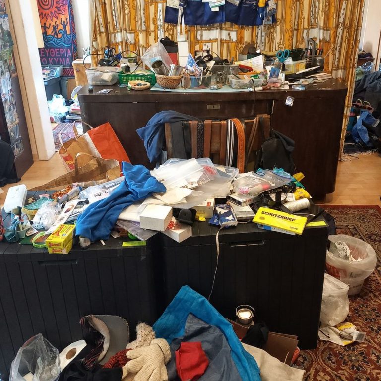 Schreibtisch Vorher I achtsames Ordnen Unordentliches Zimmer mit mehreren Gegenständen auf dem Boden und einem überladenen Schreibtsich.